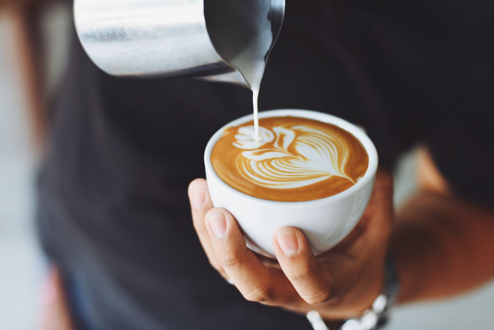 A barista pouring steamed milk into a flat white, drawing a leaf into the crema