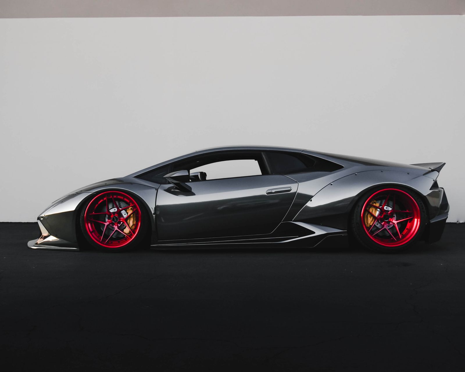 Grey Lamborghini Huracan with crimson wheels in a dark studio