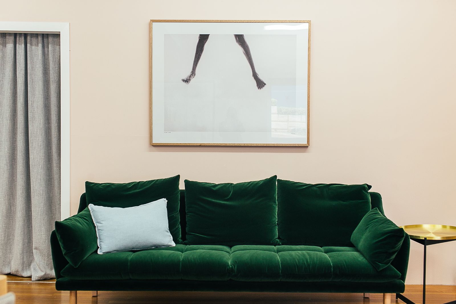A deep green velvet sofa under framed photography against a blush pink wall