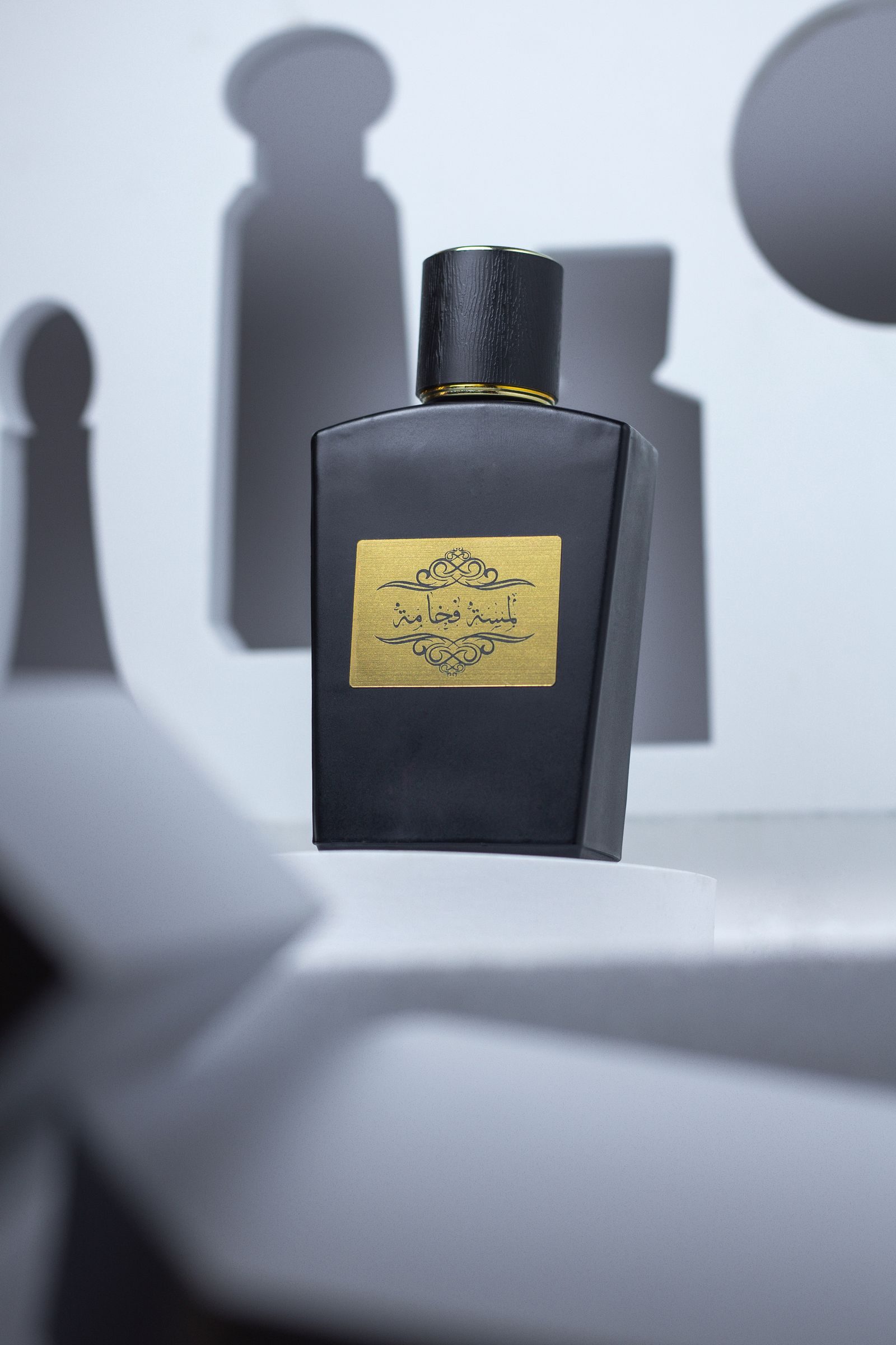 A matte black oud bottle with a gold engraved plaque, lit with sculptural shadows