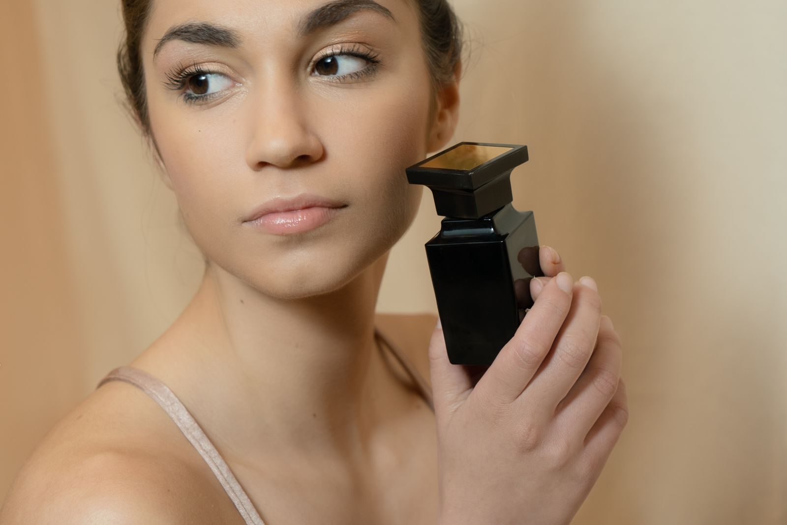 A woman holding a dark perfume bottle close to her cheek in warm light