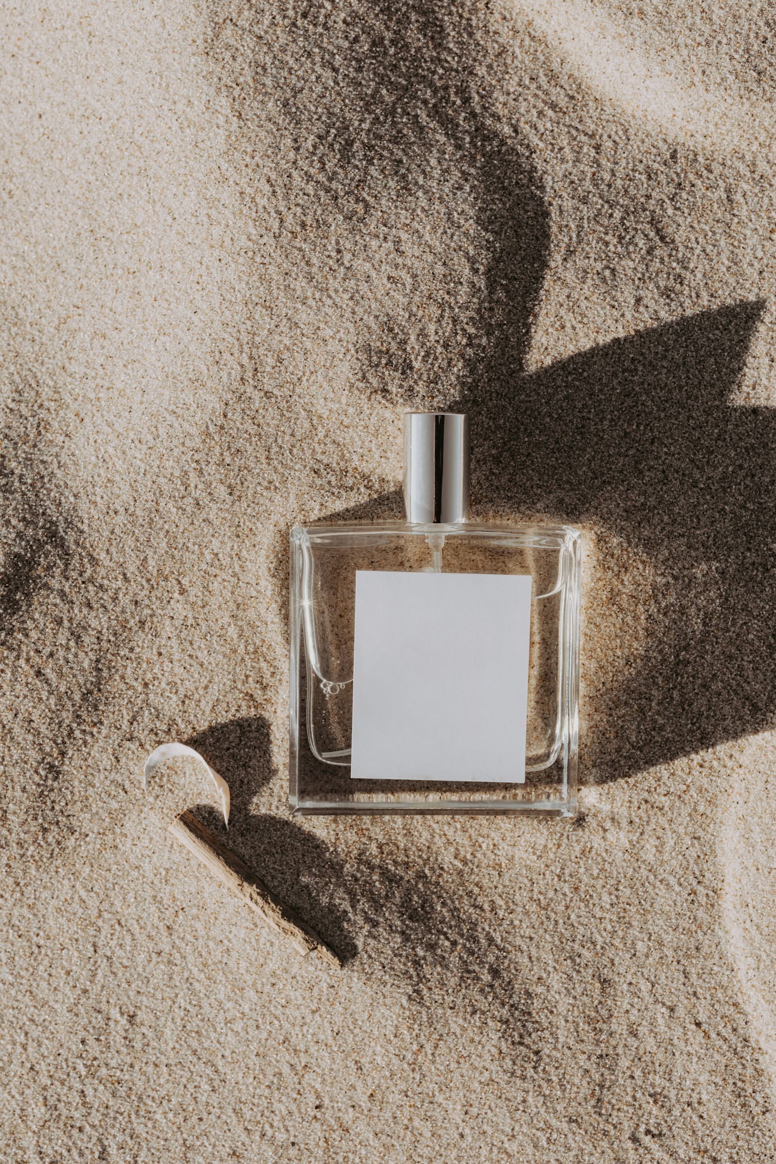 A minimalist perfume bottle half buried in warm desert sand, casting a soft shadow
