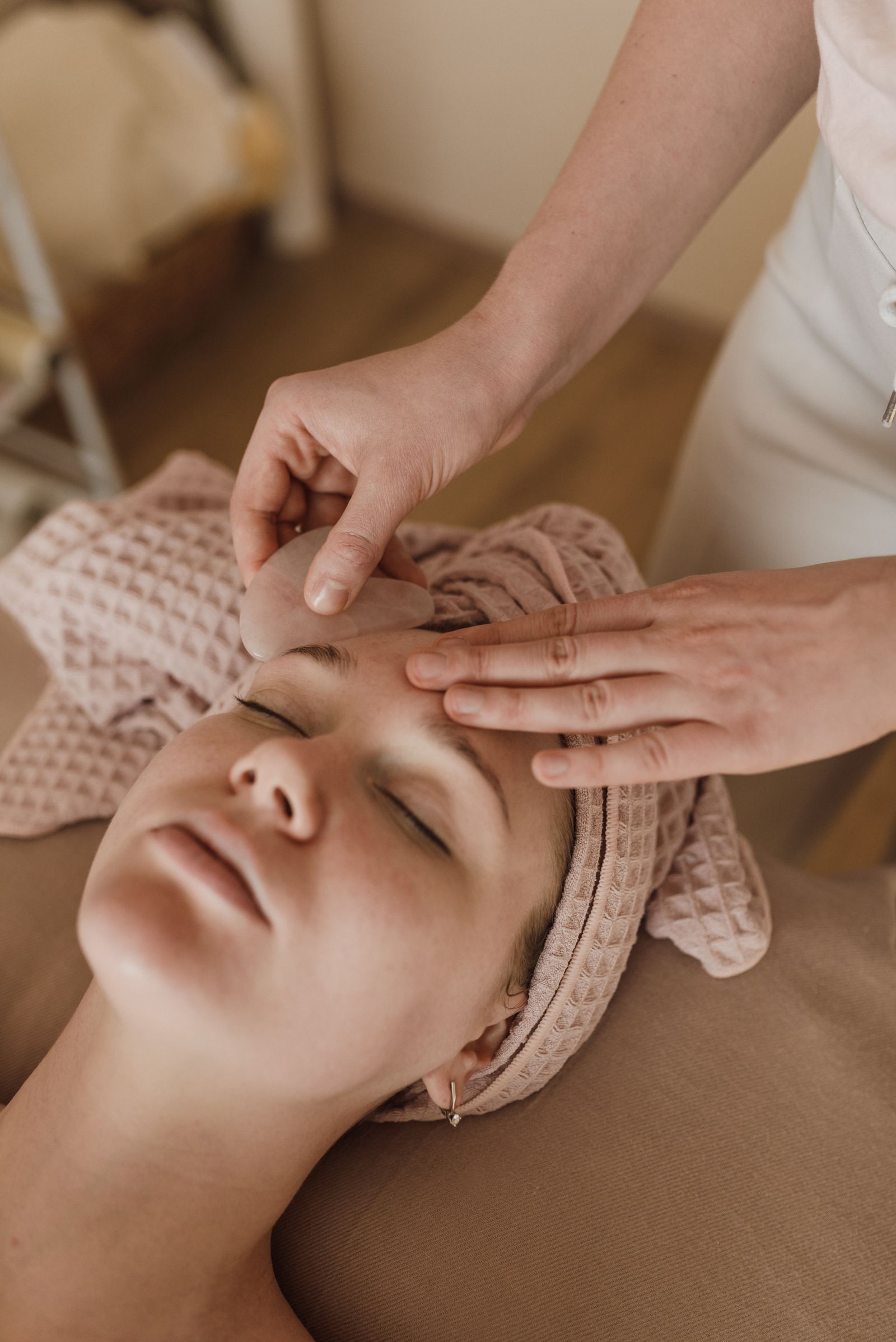 Therapist performing a rose quartz gua sha facial on a relaxed client at VELA